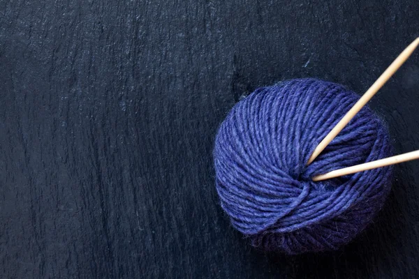 Skein of purple yarn with bamboo knitting needles with black slate background Royalty Free Stock Images