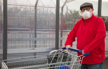 Son sınıf öğrencisi, marketten alışveriş arabasını iterken N95 maskesi takıyor. Adam kendini koronavirüsten ve diğer havadan yayılan parçacıklardan ve hastalıklardan koruyor.. 
