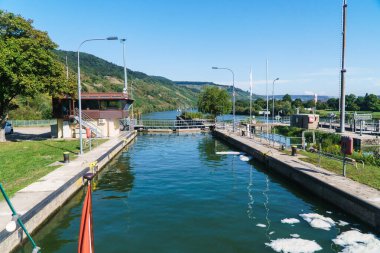 Etrafı yemyeşil tepeler ve üzüm bağlarıyla çevrili, Moselle nehrindeki bir kanala giren bir geminin manzarası.