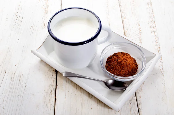 Cold milk in a enamel cup and cocoa in a glass bowl — Stock Photo, Image