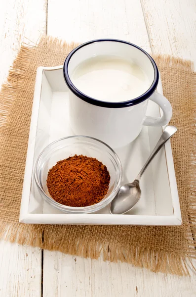 Cold milk in a enamel cup and cocoa in a glass bowl — Stock Photo, Image