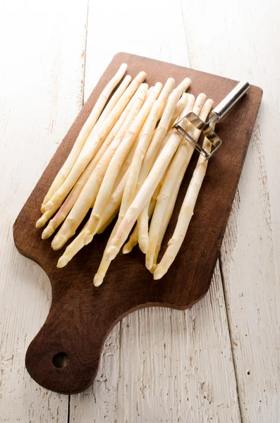 Asperges blanches et éplucheurs de légumes sur une planche en bois — Photo