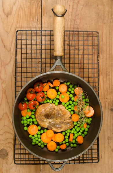 Pork neck steak with peas and carrots in a cast iron pan — Stock Photo, Image