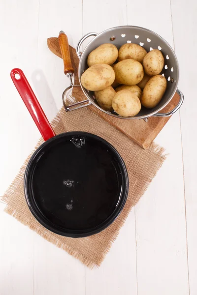 Patate pulite in un colino e pentola con acqua fredda per cucinare t — Foto Stock