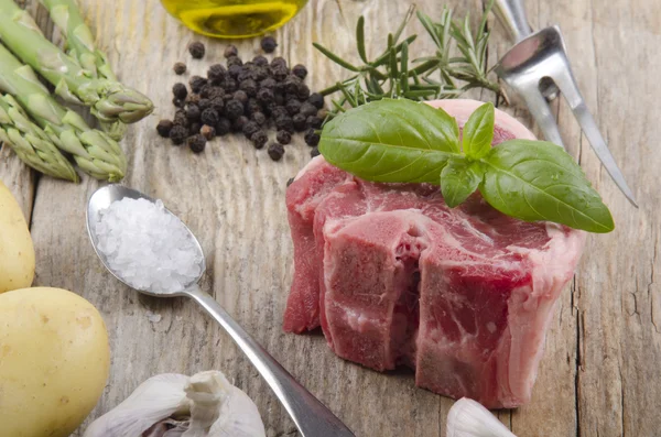 Raw lamb chop with basil on rustic wooden table — Stock Photo, Image