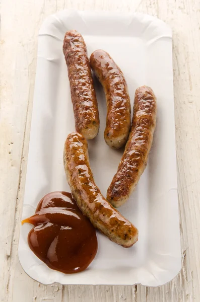 Grilled sausages with ketchup on a square paper plate — Stock Photo, Image