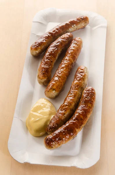 Spicy grilled sausages with mustard on a square paper plate — Stock Photo, Image