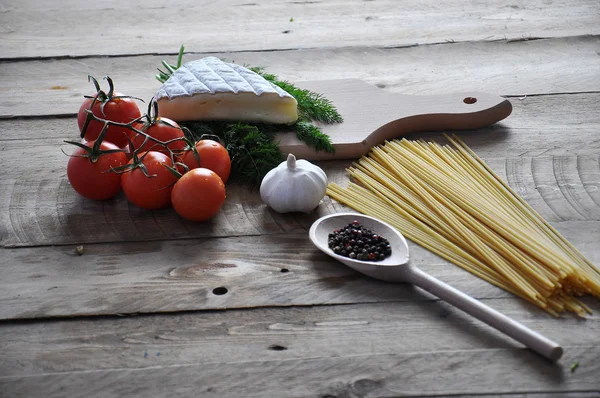 Brie cheese on a board with spaghetti and tomato on wood background — Stock Photo, Image