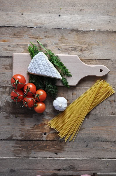 Brie cheese on a board with spaghetti and tomato on wood background — Stock Photo, Image