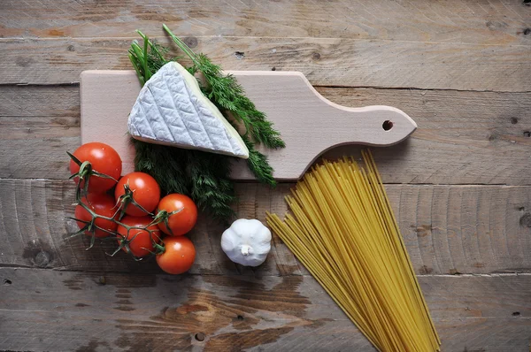 Queijo Brie em uma placa com espaguete e tomate em fundo de madeira Imagem De Stock