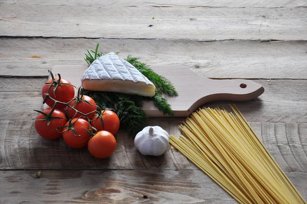 Queijo Brie em uma placa com espaguete e tomate em fundo de madeira Imagem De Stock