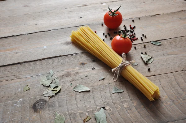 Cooking concept. Uncooked italian pasta: vermicelli, spaghetti with twine and tomato on wooden background — Stock Photo, Image