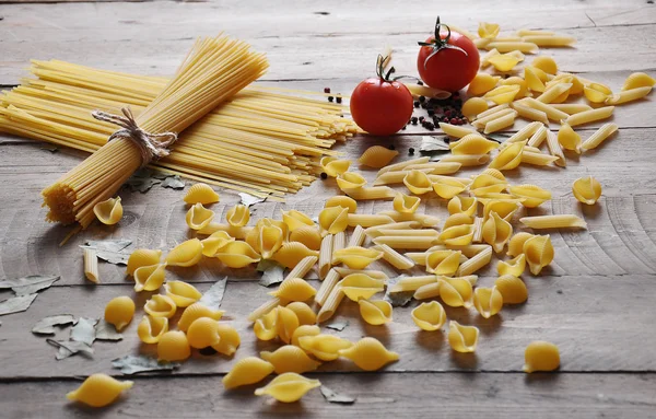 Pişirme kavramı. Pişmemiş makarna çeşitleri: erişte, spagetti sicim ve ahşap zemin üzerine domates ile — Stok fotoğraf