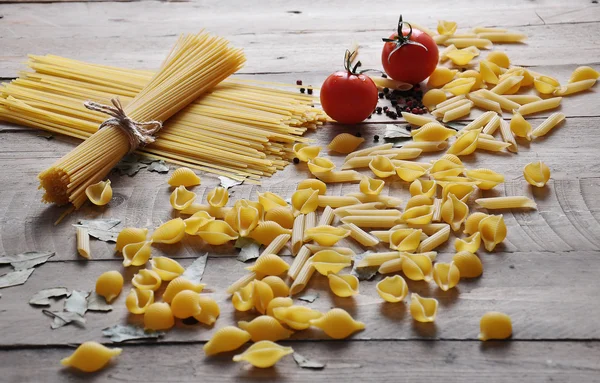 Cooking concept. Uncooked italian pasta: vermicelli, spaghetti with twine and tomato on wooden background — Stock Photo, Image