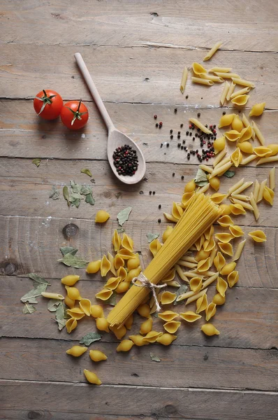 Vaření koncepce. Italské těstoviny nevařené: nudle, špagety s provázkem a rajče na dřevěné pozadí — Stock fotografie