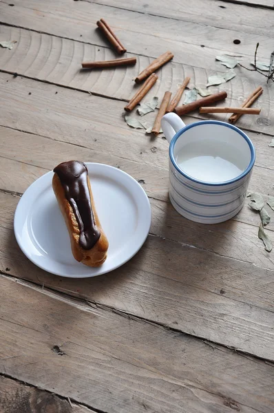 Exquisite Sahnedessert Eclair bestreut mit Schokolade und Milch auf dem Holz — Stockfoto