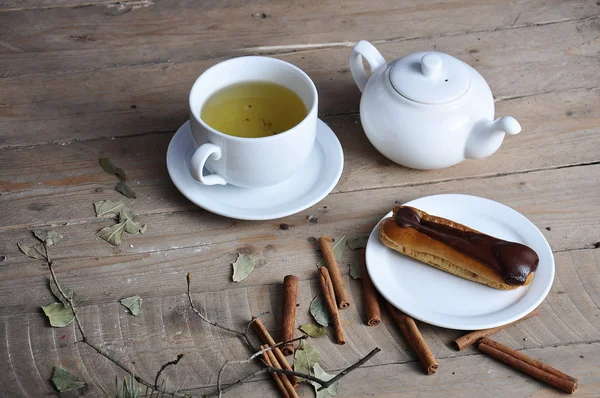 Exquisito postre crema eclair espolvoreado con chocolate y té en la madera —  Fotos de Stock