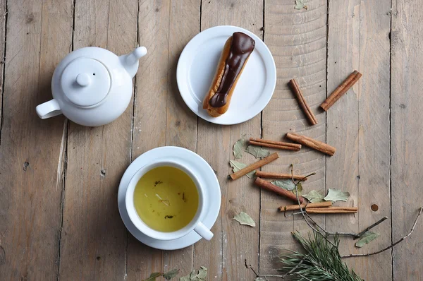 Exquisito postre crema eclair espolvoreado con chocolate y té en la madera —  Fotos de Stock