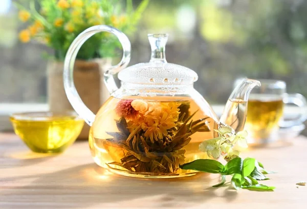 Glass tea teapot with a blooming tea flower stands on the table in the rays of the su