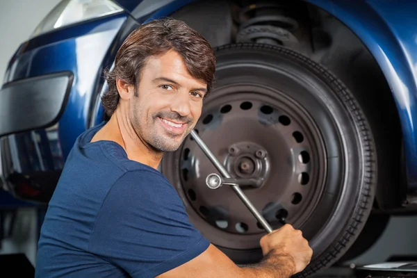 Lächelnder Mechaniker fixiert Autoreifen mit Felgenschlüssel — Stockfoto