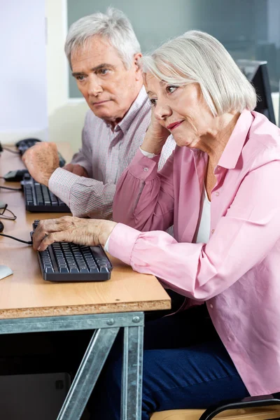 Femme âgée ennuyée utilisant un ordinateur avec un camarade de classe masculin — Photo