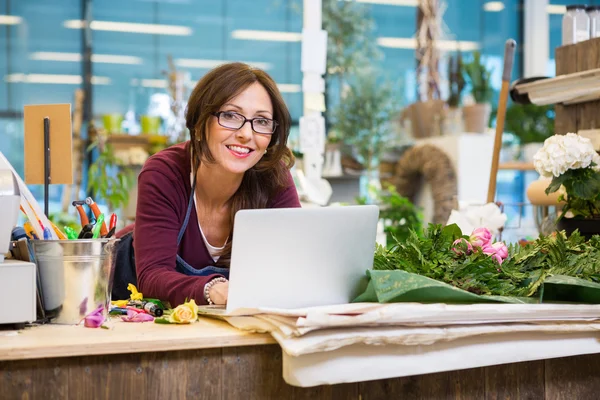 Florista usando el ordenador portátil en el mostrador en la tienda de flores —  Fotos de Stock