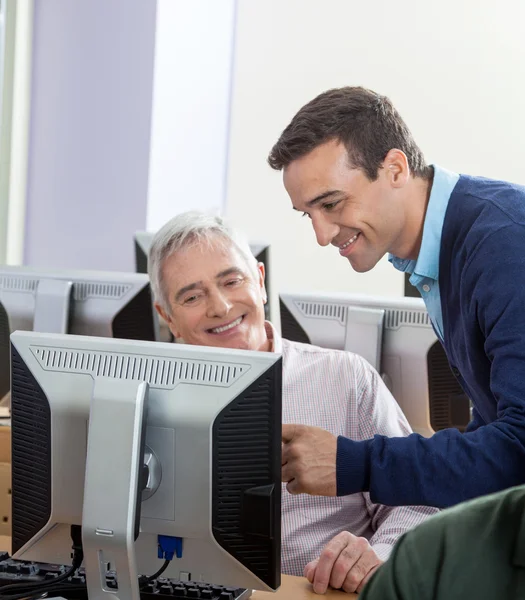 Istruttore felice che assiste l'uomo anziano alla scrivania del computer — Foto Stock