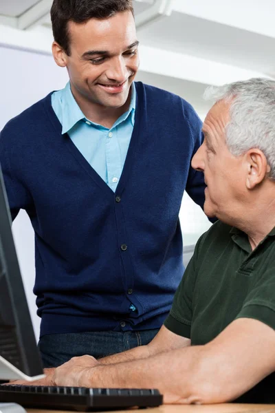 Lächelnder Nachhilfelehrer schaut Oberschüler im Computerkurs an — Stockfoto