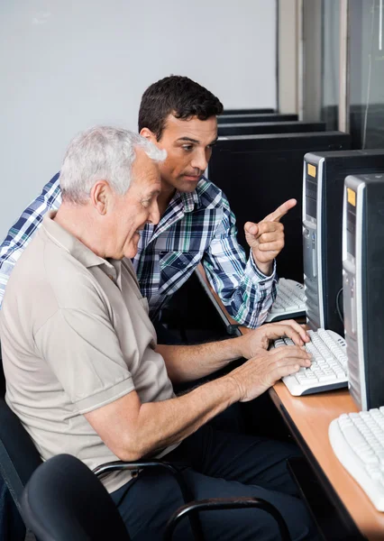 Tutor ajudando o homem sênior no uso de computador — Fotografia de Stock