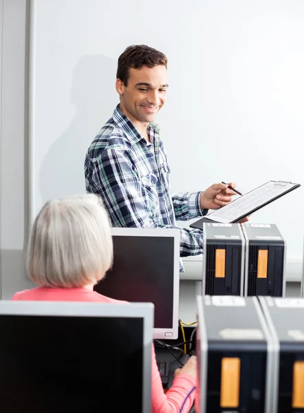 Jovem Tutor feliz segurando prancheta na classe de computador — Fotografia de Stock