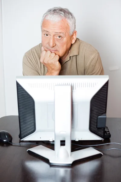 Homme âgé sérieux assis au bureau de l'ordinateur en classe — Photo