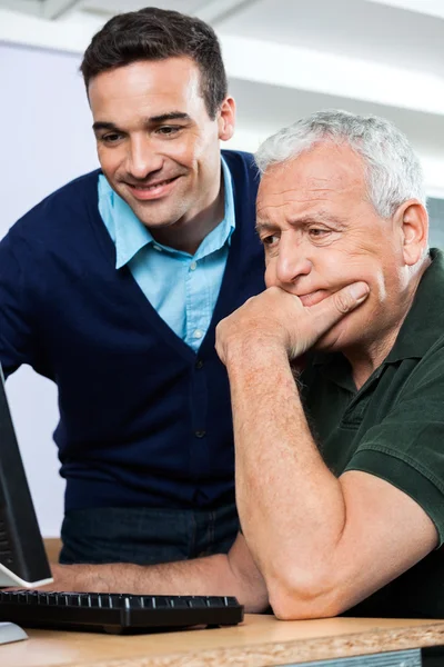 Professor sorridente ajudando o homem sênior no uso de computador — Fotografia de Stock