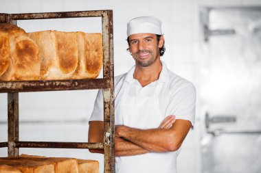 Erkek Baker ayakta silah ekmek raf tarafından geçti gülümseyen
