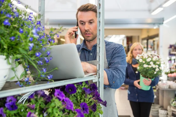 Florista usando el teléfono móvil y el ordenador portátil en la tienda — Foto de Stock