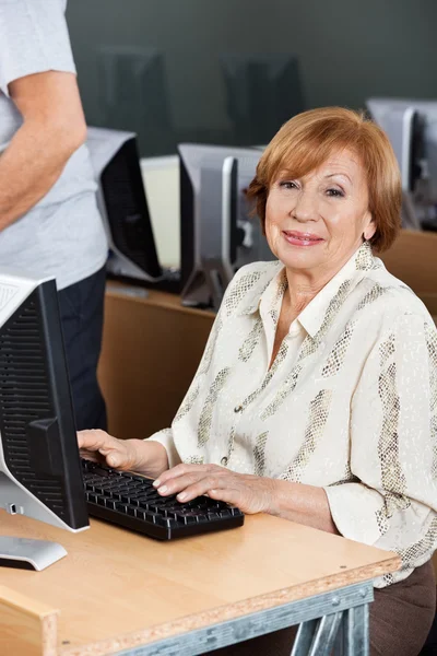 Gelukkig Senior vrouw met behulp van Computer op Bureau In de klas — Stockfoto