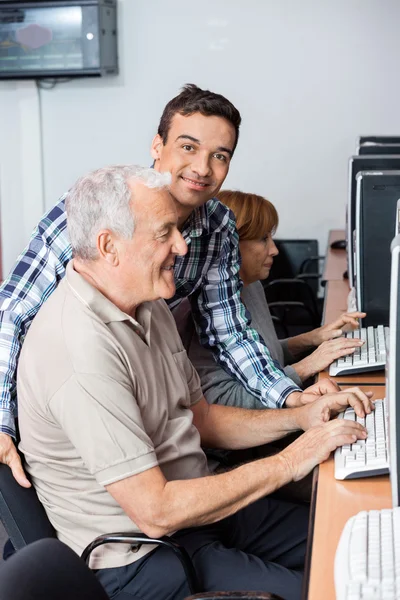 Tutor ajudando o homem sênior no uso de computador — Fotografia de Stock