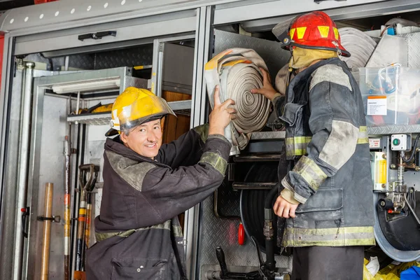 Lächelnder Feuerwehrmann hilft Kollege beim Entfernen von Schlauch — Stockfoto