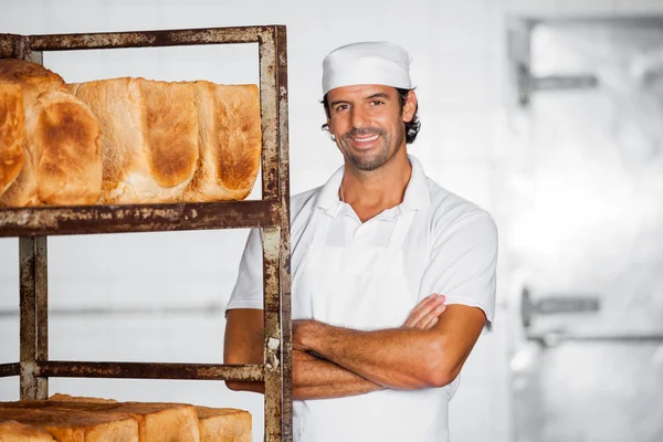 Sorrindo Masculino Baker Braços em pé Cruzados pela cremalheira do pão — Fotografia de Stock