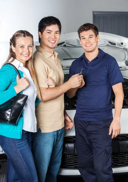 Felice coppia dando chiavi auto al tecnico — Foto Stock