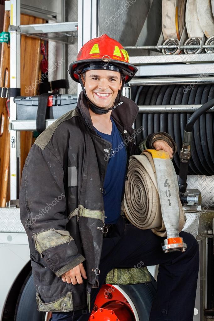 Счастливый пожарный держит шланг, стоя у грузовика стоковое фото ...