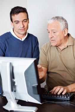 Bilgisayar monitöründe doğru işaret ederken öğretmen ile konuşan adam