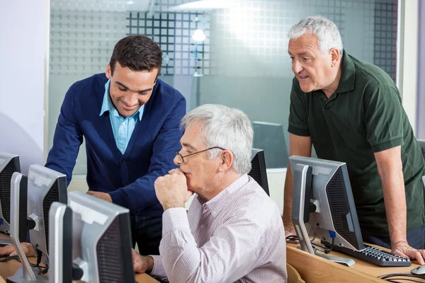 Instructor feliz explicando a los hombres mayores en clase de informática — Foto de Stock