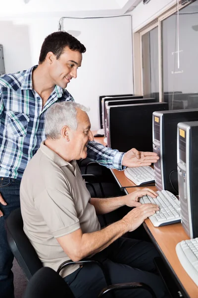 Tutor Assistindo o homem sênior no uso de computador — Fotografia de Stock