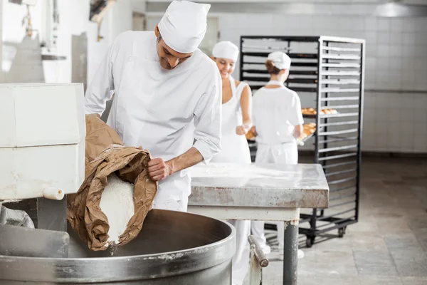 Reifer männlicher Bäcker gießt Mehl in Knetmaschine — Stockfoto