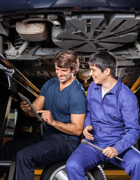 Glückliche Mechaniker mit digitalem Tablet unter dem Auto — Stockfoto