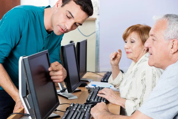 Tutor orientando os alunos seniores no uso de computador na sala de aula — Fotografia de Stock