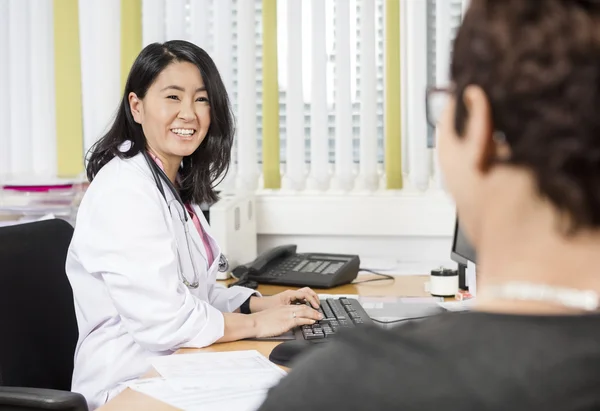 Doctor feliz usando la computadora mientras mira al paciente en el escritorio —  Fotos de Stock