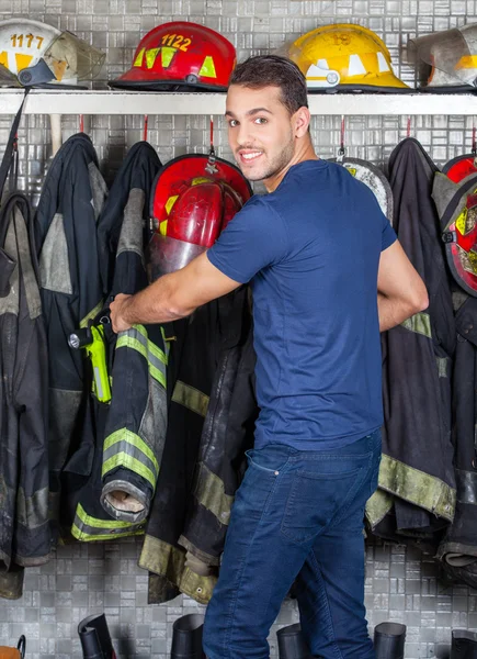 Lächelnder Arbeiter entfernt Uniform, die am Feuerwehrhaus hängt — Stockfoto