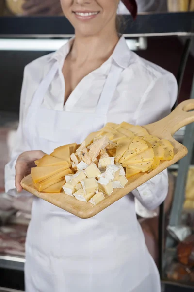 Vendedora segurando placa de corte com queijo sortido — Fotografia de Stock
