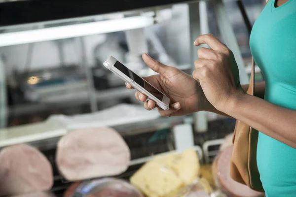 Mulher usando telefone celular na loja de queijo — Fotografia de Stock